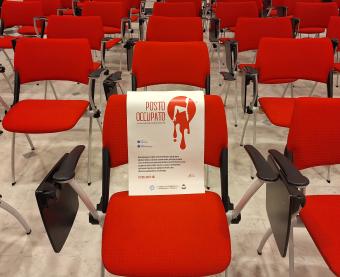 Immagine della sedia vuota con la locandina della campagna 'Posto occupato' nella sede della Camera di Commercio Maremma e Tirreno